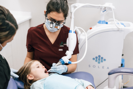 A dentist treats a child with a dental laser.